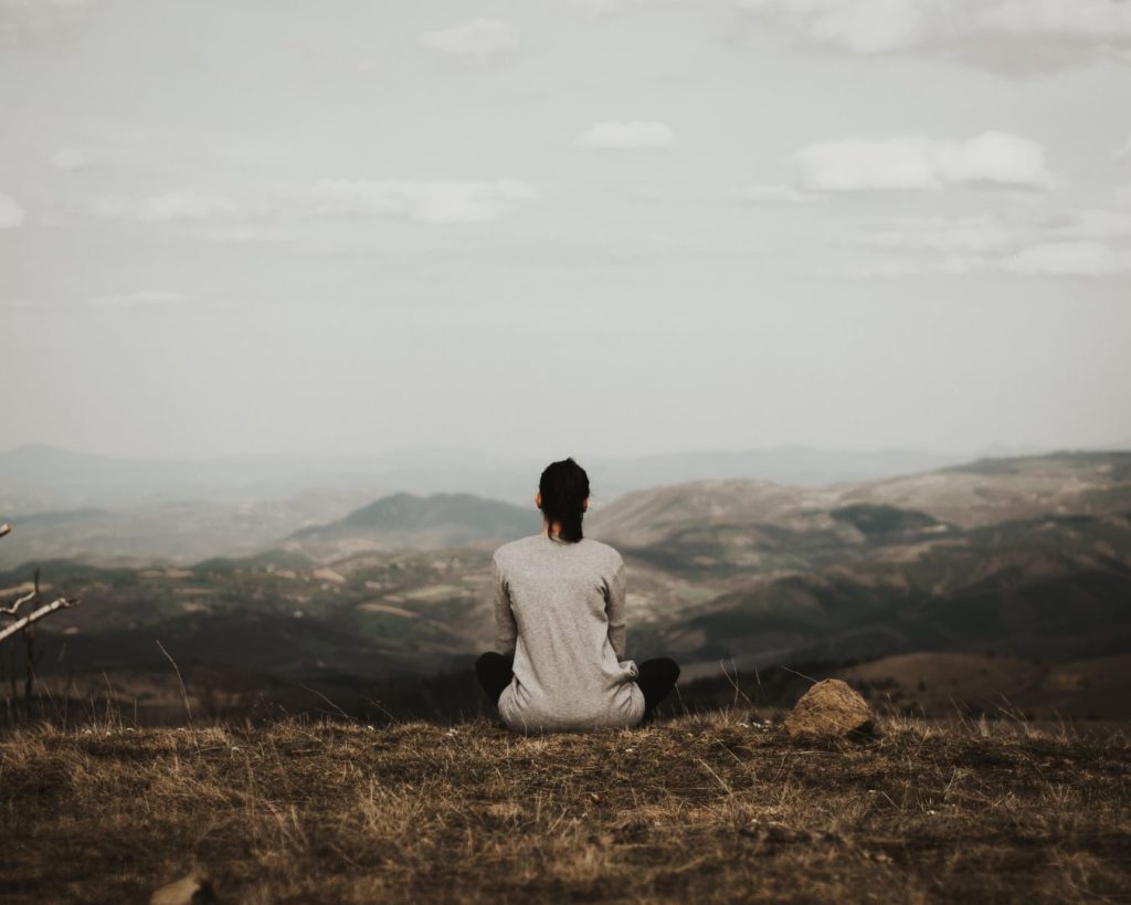 Girl sitting on the a hill overlooking mountains and reflecting