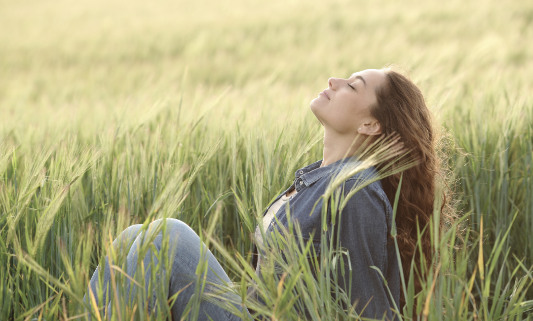 woman sitting in field feeling the sun and wind