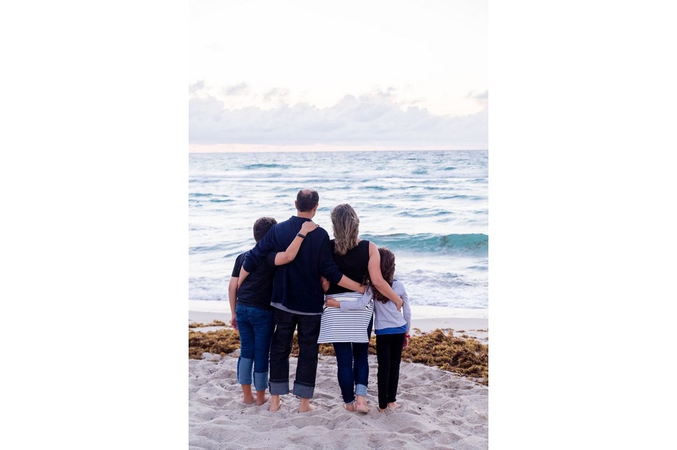 family of four hugging, blue jeans, striped sweater, sand, beach, ocean, dead seaweed
