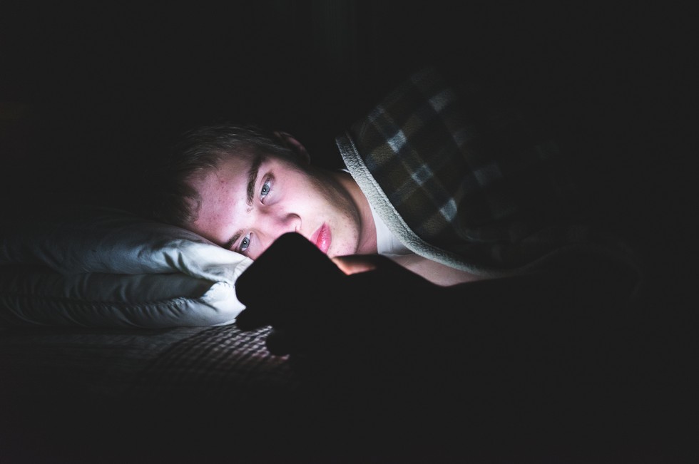 Teenager laying in bed in the dark on smartphone 