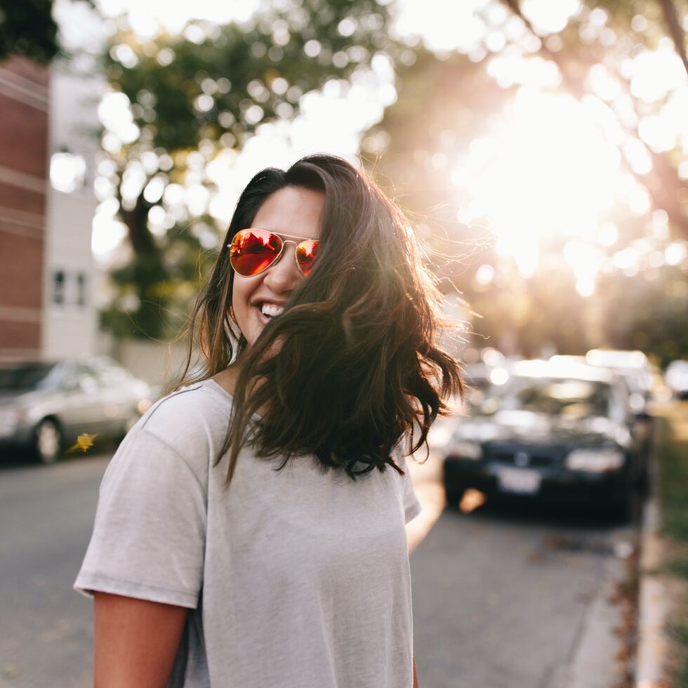 girl smiling outside, residential street, sun in the trees, gray shirt, mirrored sunglasses
