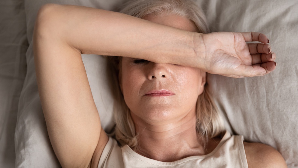 Woman in menopause in bed with arm over eyes to show lack of sleep