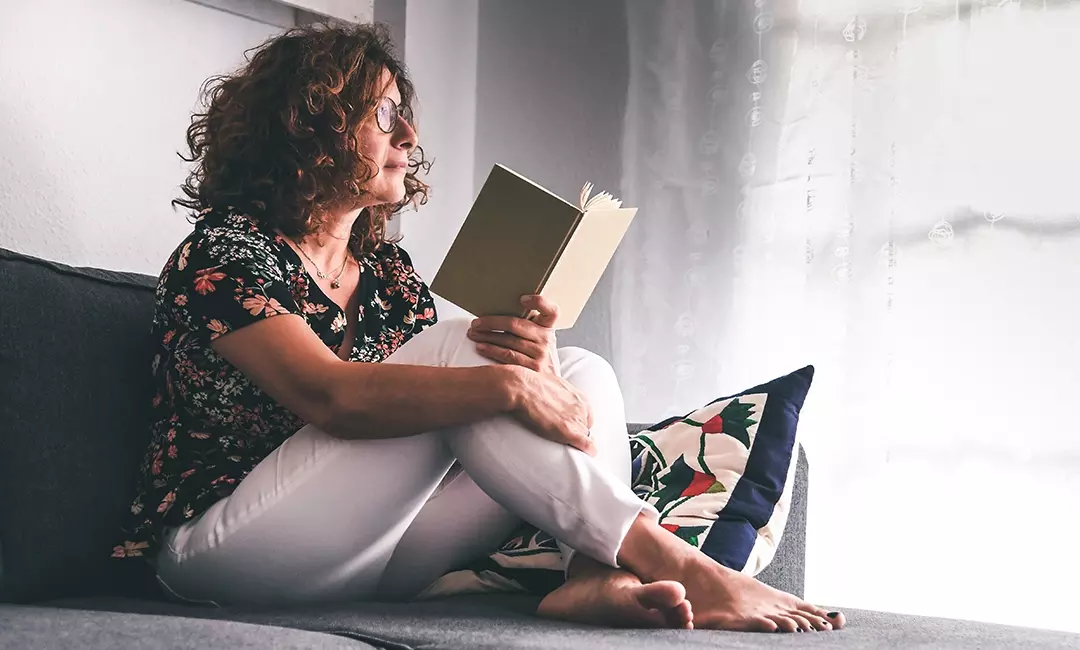Woman sitting on couch reading book inventively
