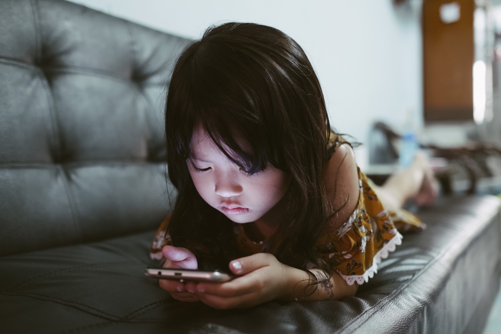 School age child on smartphone while lying on couch