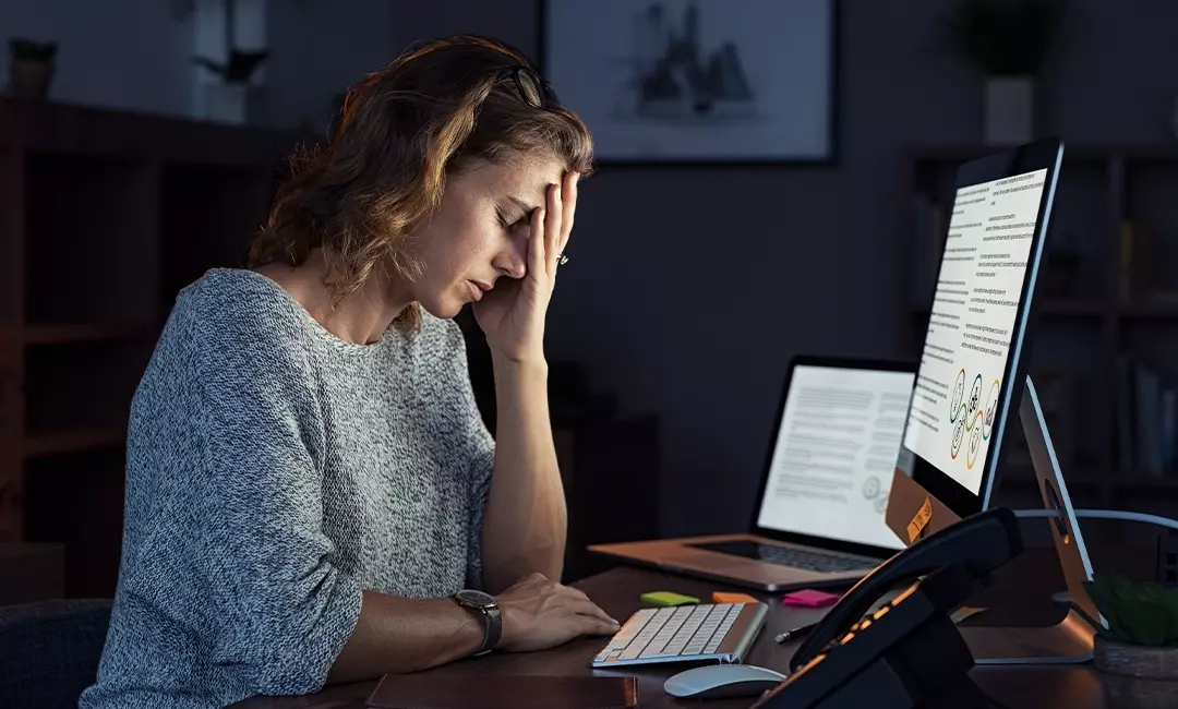 Woman working on laptop in dark burnt out and tired